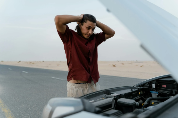 A person standing by an overheated car on the side of the road.